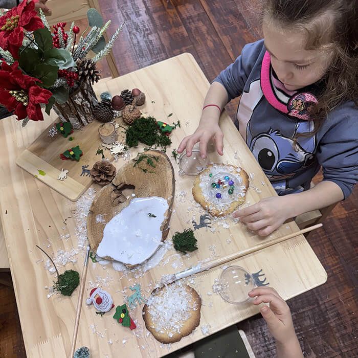 Mini Masterminds Child Care A girl sitting at a table with a table full of objects.